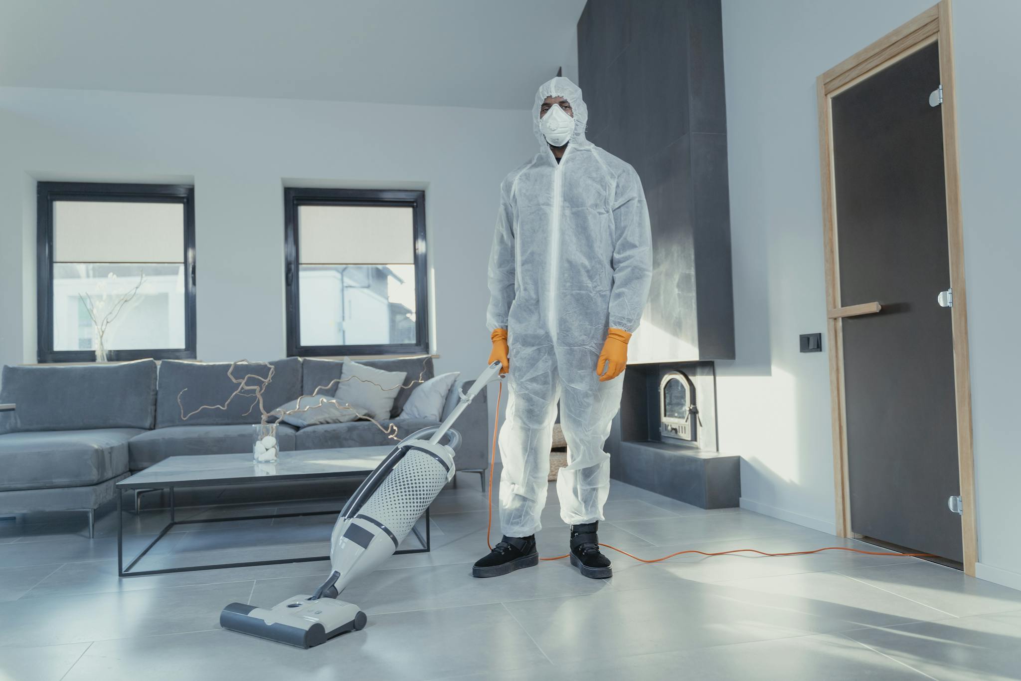 A person in protective coveralls vacuuming a contemporary living room.