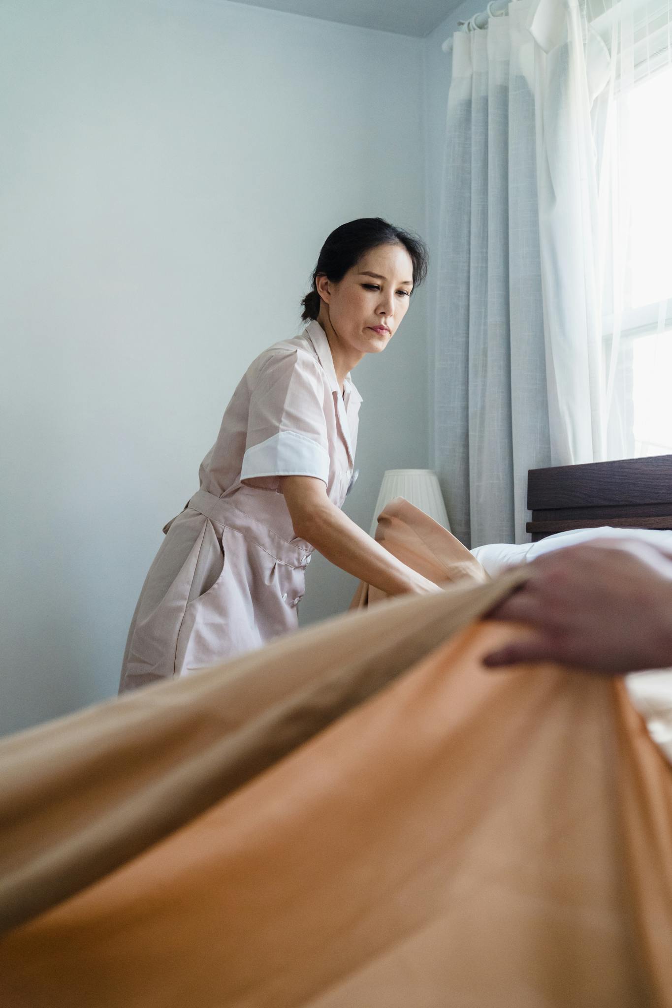 An adult woman tidying up a bed in a bright bedroom, showcasing meticulous housekeeping.