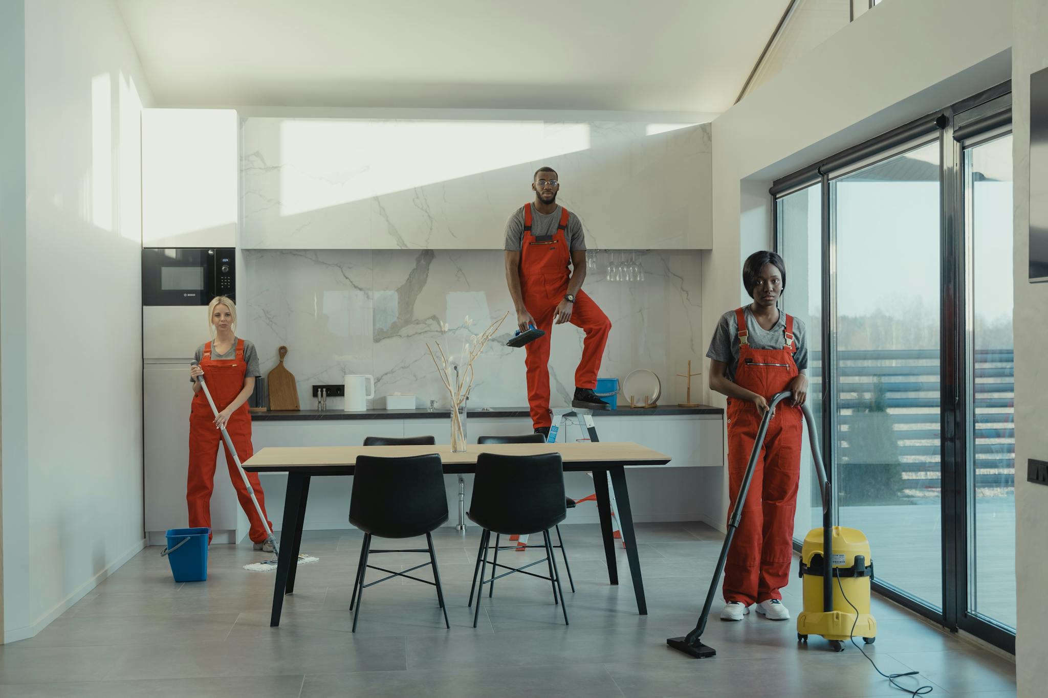 Three cleaning staff working in a contemporary kitchen setting, showing teamwork and efficiency.